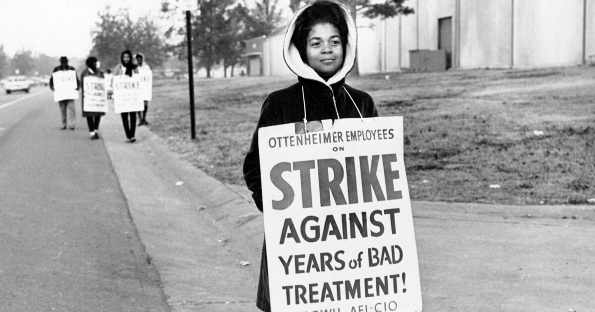 A woman holds a sign that says Strike Against Years of Bad Treatment.