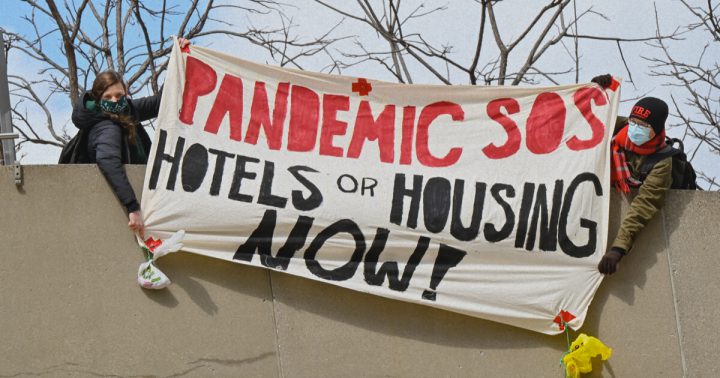 Protesters hold up a banner that says "Pandemic SOS: Hotels or Housing Now!"