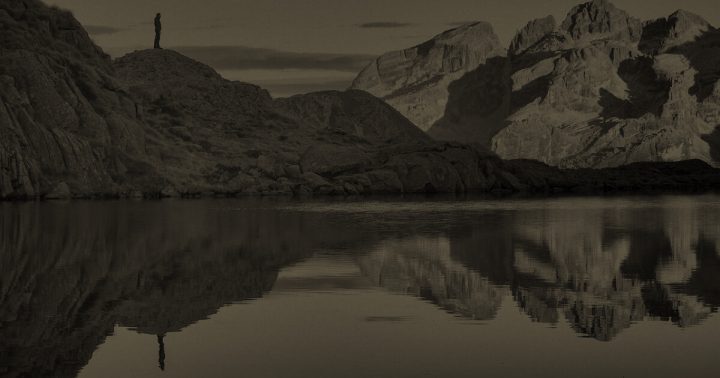 Hiker and mountains reflected in water